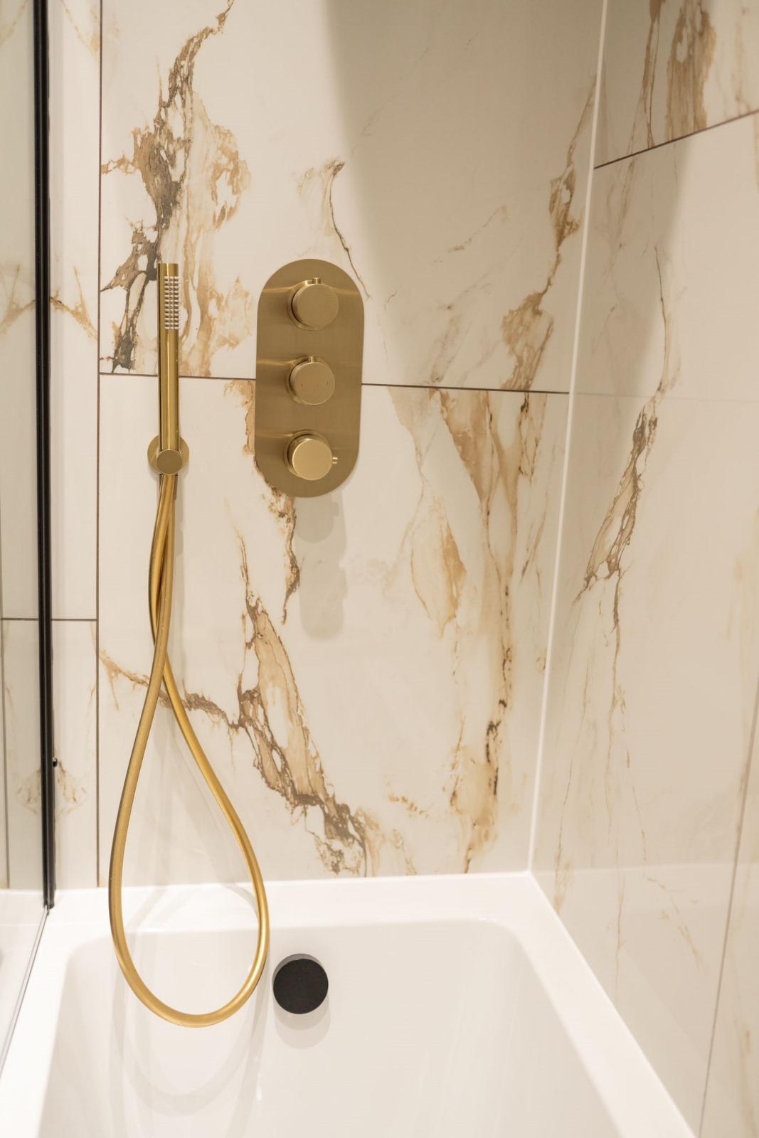 Brushed brass shower controls on marble tile