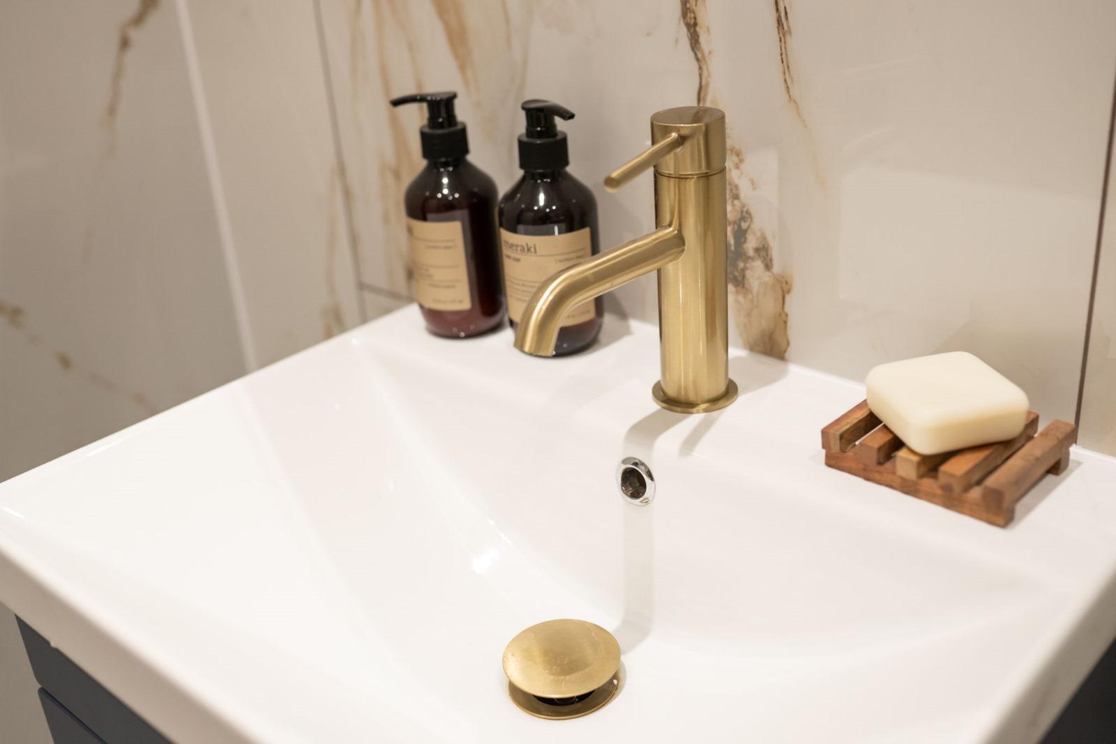 Brass mixer tap on white basin with marble background
